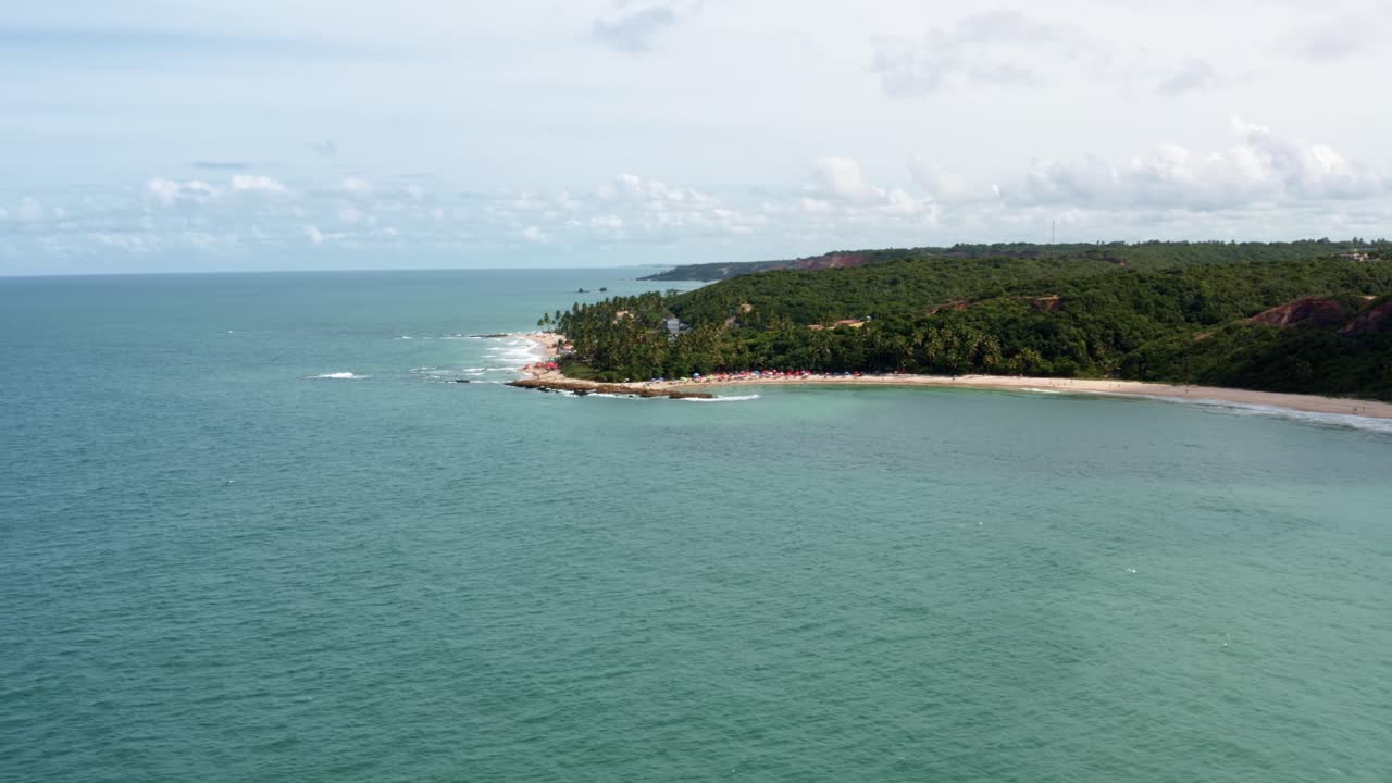 dolly en un dron aéreo de gran amplitud de la popular playa tropical de coquerinhos cubierta de paraguas con turistas nadando en una piscina natural de un arrecife en condé, paraíba, brasil