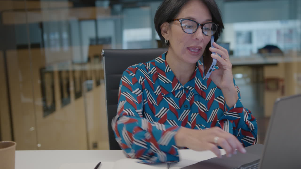 Mature Businesswoman Using Laptop and Speaking on Phone in Office