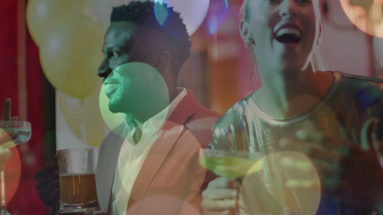 Kvinde i metallisk top holder tale med en drink i hånden, kameraet zoomer ud, bokeh-effekt på drinks, skåler ved et arrangement.