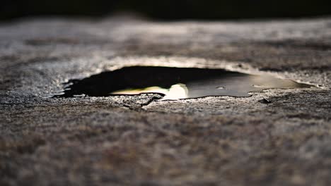 a dark reflection of the setting sun in a small puddle on a grey stone with bright yellow light and sharp surface texture