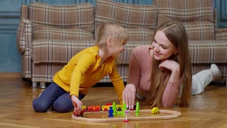 Mother-playing-with-child-kid-daughter-riding-toy-train-on-wooden-railroad-blocks-board-game-at-home