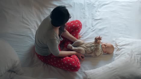 woman in sleepwear with adorable child on bed. loving mom playing with baby boy