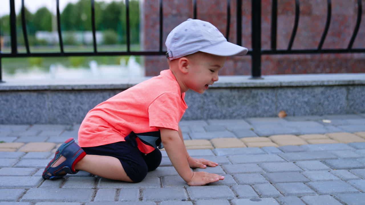 Funny toddler boy crawling by the paved road in the park. Cheerful kid having fun outdoors in summer.