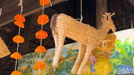 a woven animal figure and orange hanging decorations inside a pavilion with a colorful mural backdrop.