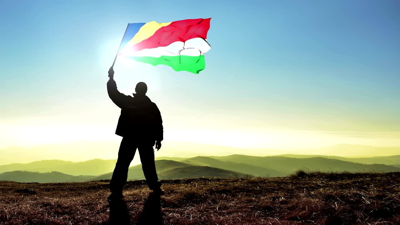 Erfolgreiche Silhouette eines Siegers, der die Flagge der Seychellen auf dem Berggipfel schwenkt. Cinemagraph LOOP Hintergrund.