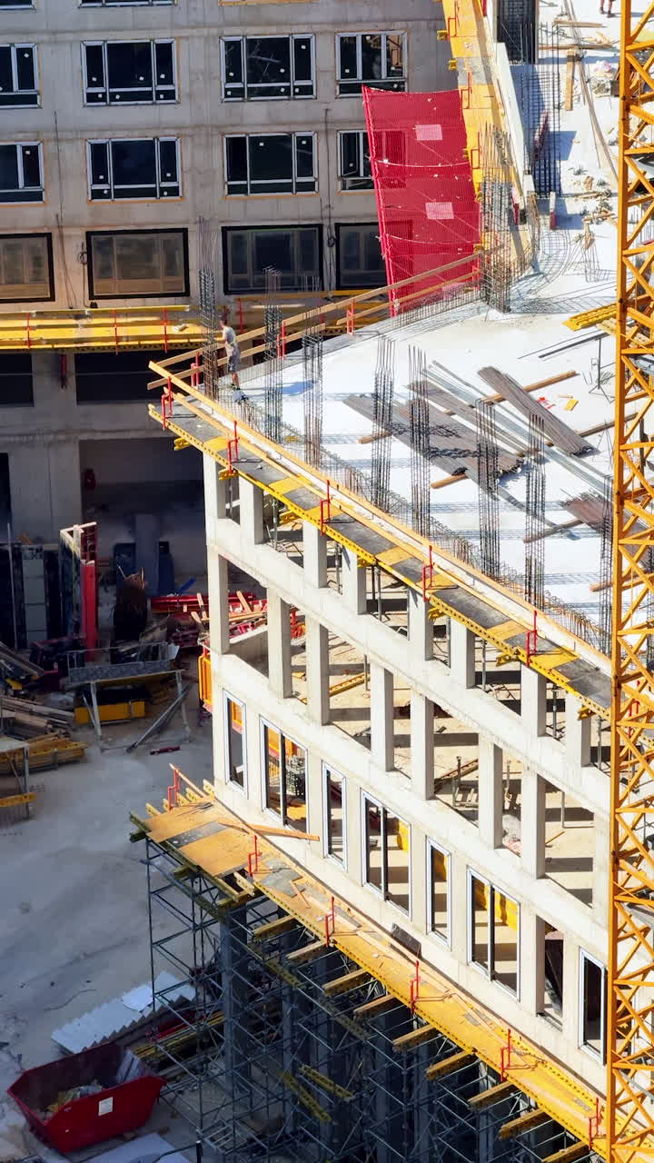 Commercial building progress. Workers and machinery are busy at a construction site, with scaffolding and concrete structures visible during daylight
