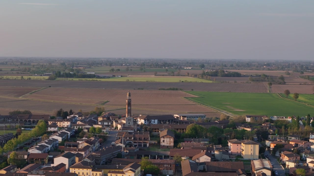 Il villaggio di Spinadesco e il campanile della Chiesa di San Martino Vescovo vicino a Porto Canale nella Pianura Padana, provincia di Cremona, Lombardia, Italia, circondato da pianure agricole, ripresa panoramica laterale con drone