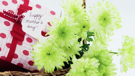 Gift-box-and-bunch-of-yellow-flowers-in-wicker-basket-with-happy-mothers-day-tag