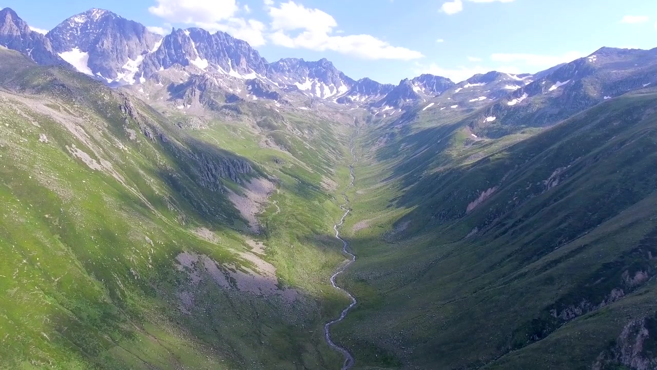 Flyfoto av en svingete bekk i en frodig fjell dal.