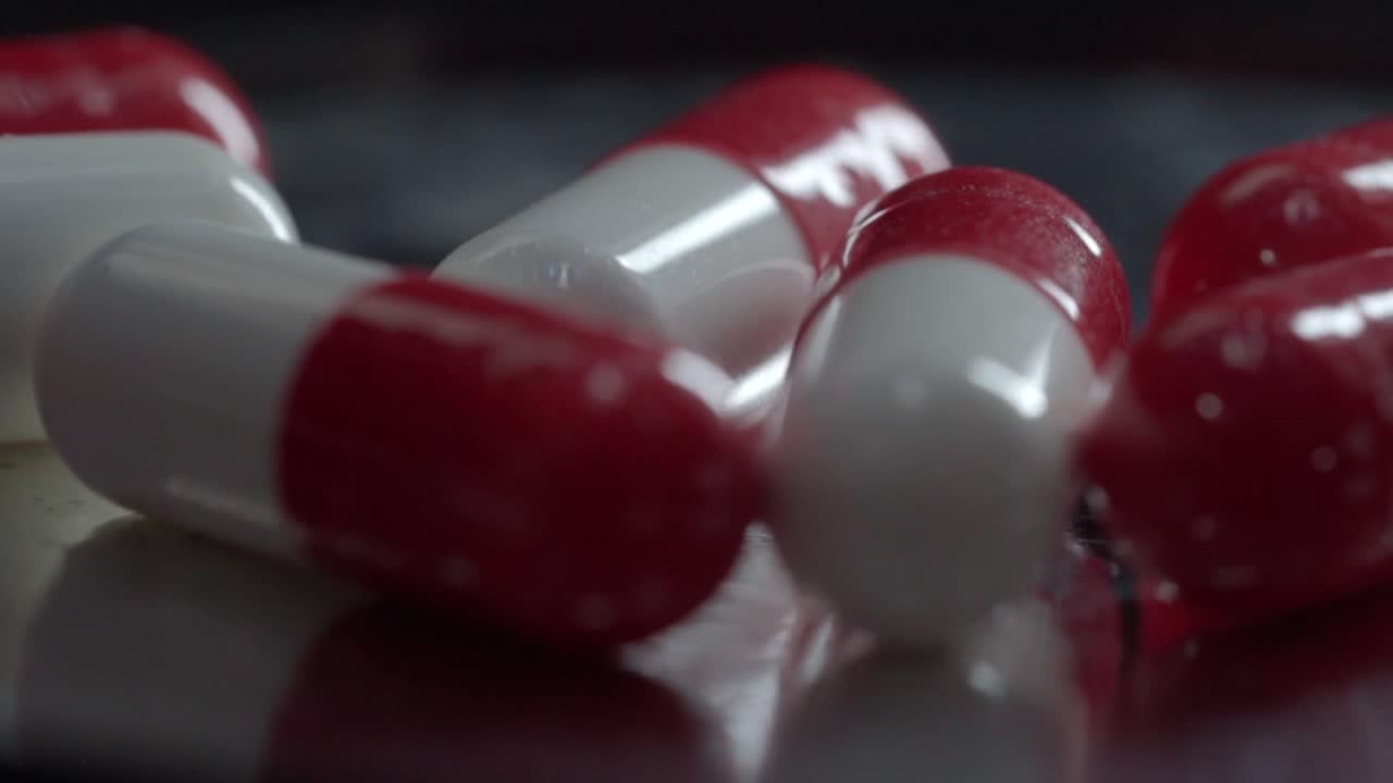 Close up of red and white pharmaceutical capsules on dark reflective surface, studio lighting