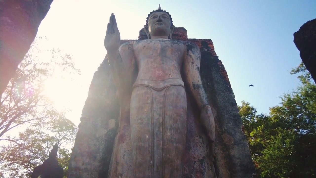 Máy quay lia lên tượng Phật đứng khổng lồ bên ngoài tàn tích cổ kính của Wat Maha That. Di sản Thế giới UNESCO.