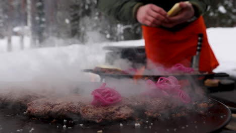 man making reindeer cheeseburgers over flaming barbeque topping with onions for snowy swedish meal