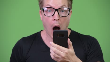 young handsome nerd man using phone looking shocked