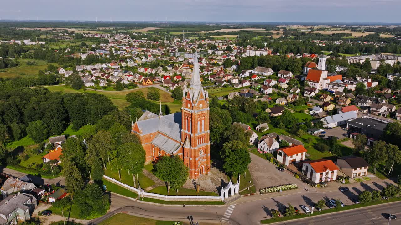 Pullback aerial shot reveals Kelmė church tower and town layout in warm daylight