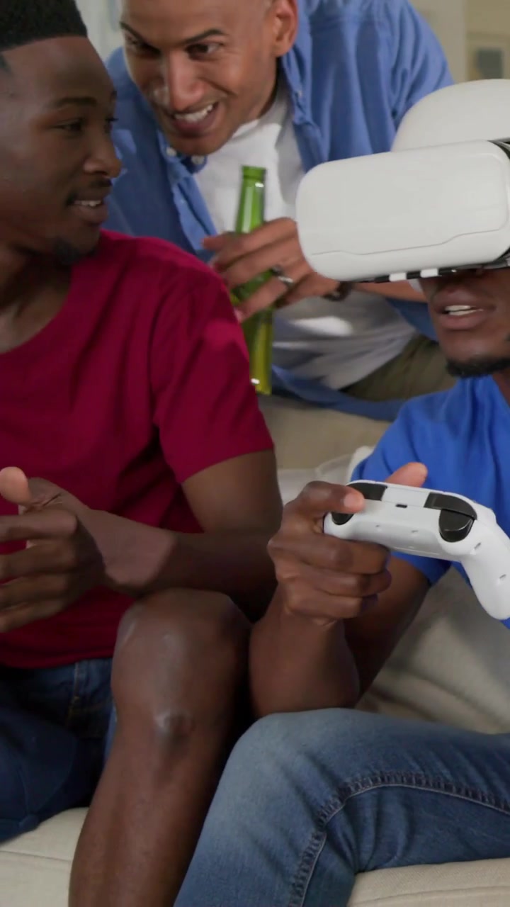 Vertical video: Starting game man in blue tee with white VR headset using gamepad on couch for fun
