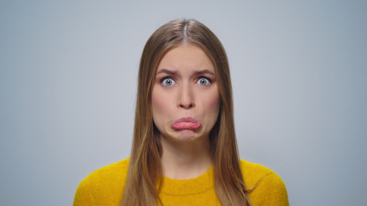 Portrait of beautiful girl making grimaces at camera on grey background.