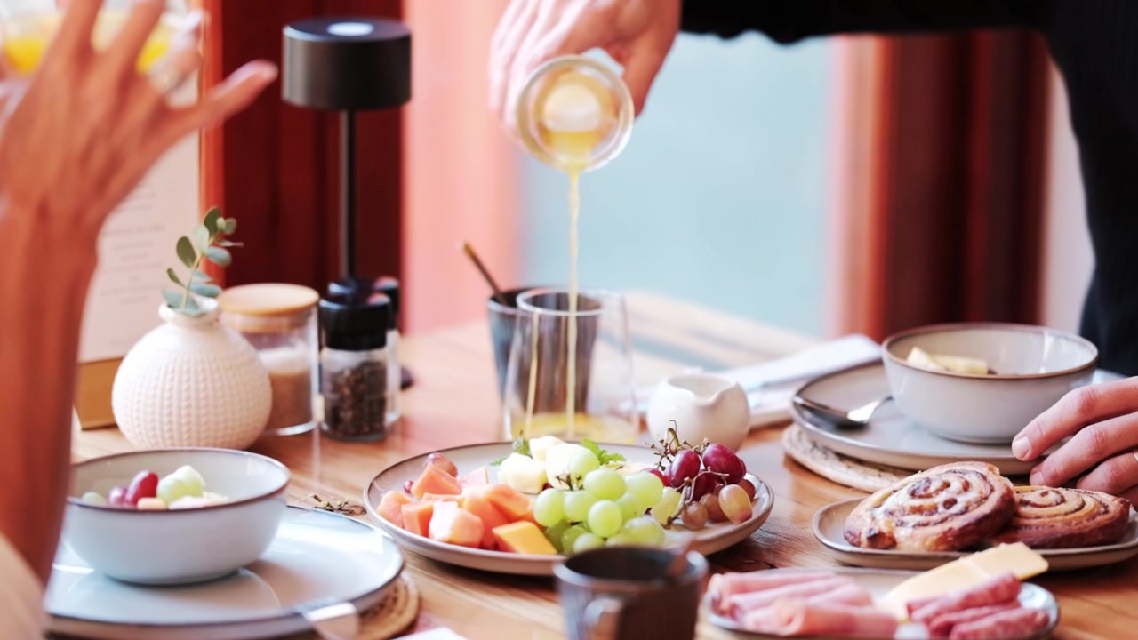 Et par nyder en morgenmadsbuffet, mens de hælder og drikker appelsinjuice.
