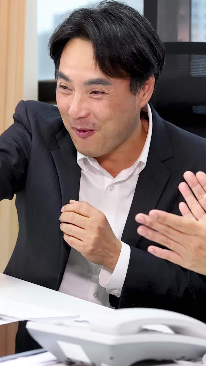 นักธุรกิจชายยิ้มแย้มปรบมืออย่างกระตือรือร้นกับเพื่อนร่วมงานระหว่างการประชุมสำนักงานที่ประสบความสำเร็จ ภายใต้แสงไฟสว่างแบบมืออาชีพ
