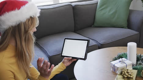 Happy-biracial-woman-wearing-santa-hat-using-tablet-at-christmas,-copy-space,-slow-motion