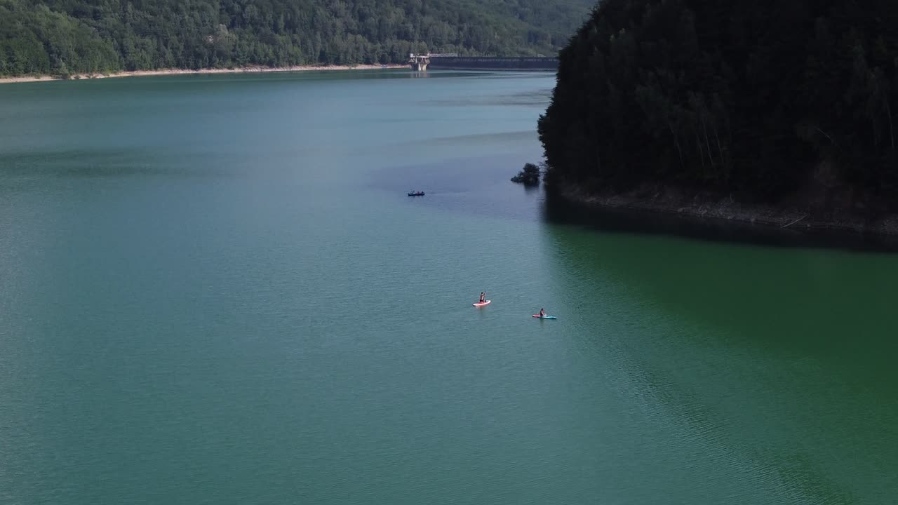 Aerial orbit shot of young couple having a relaxing afternoon on paddle boards on Paltinu lake of Doftana Valley in Romania