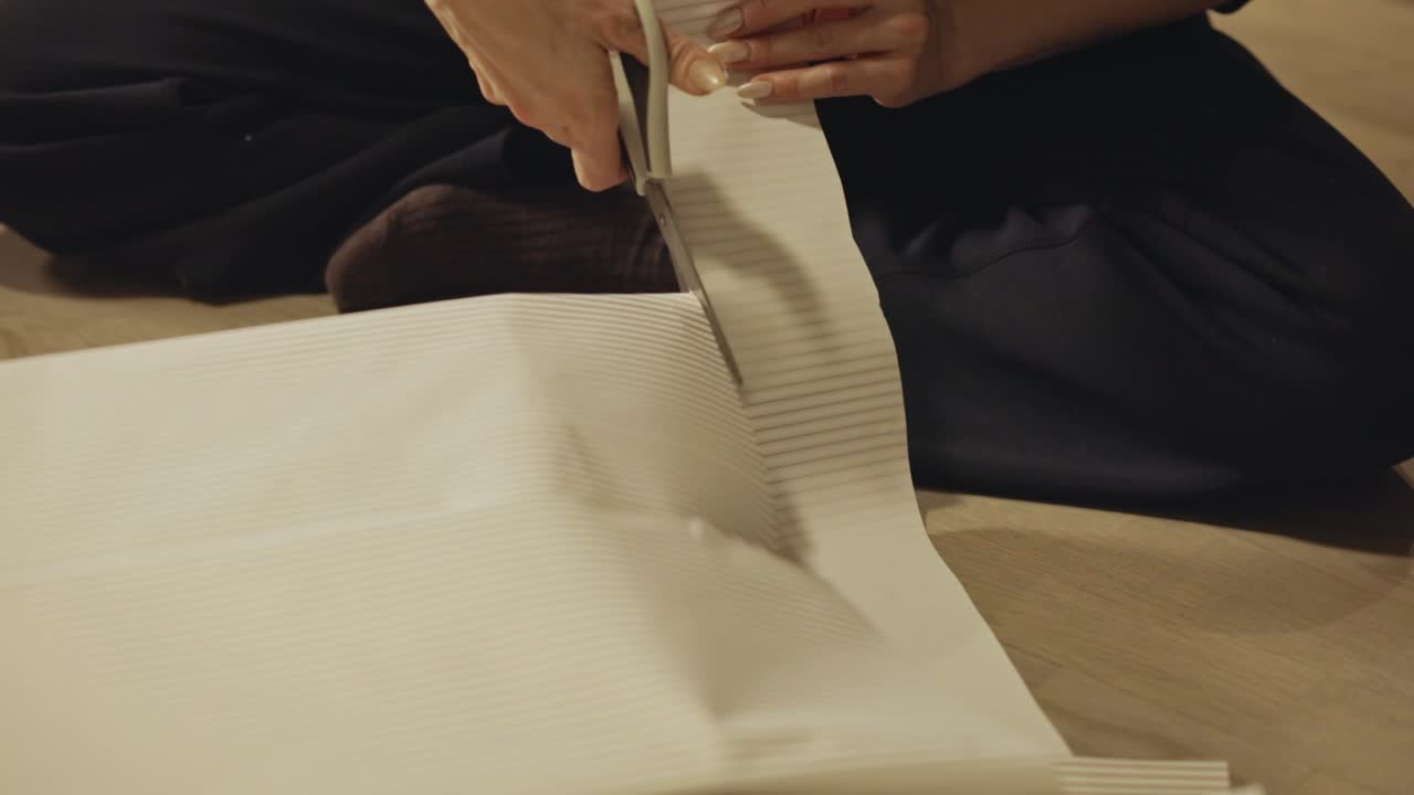 Hands Carefully Trim Striped Wrapping Paper to Neatly Finish a Christmas Gift - Close Up