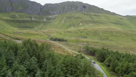 Drone-shot-of-a-car-driving-towards-Glenniff-Horseshoe,-flying-forwards-along-the-road-with-with-trees-on-either-side