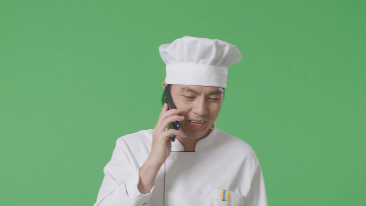 Uomo asiatico chef che parla al telefono mentre cammina in uno studio con sfondo green screen.