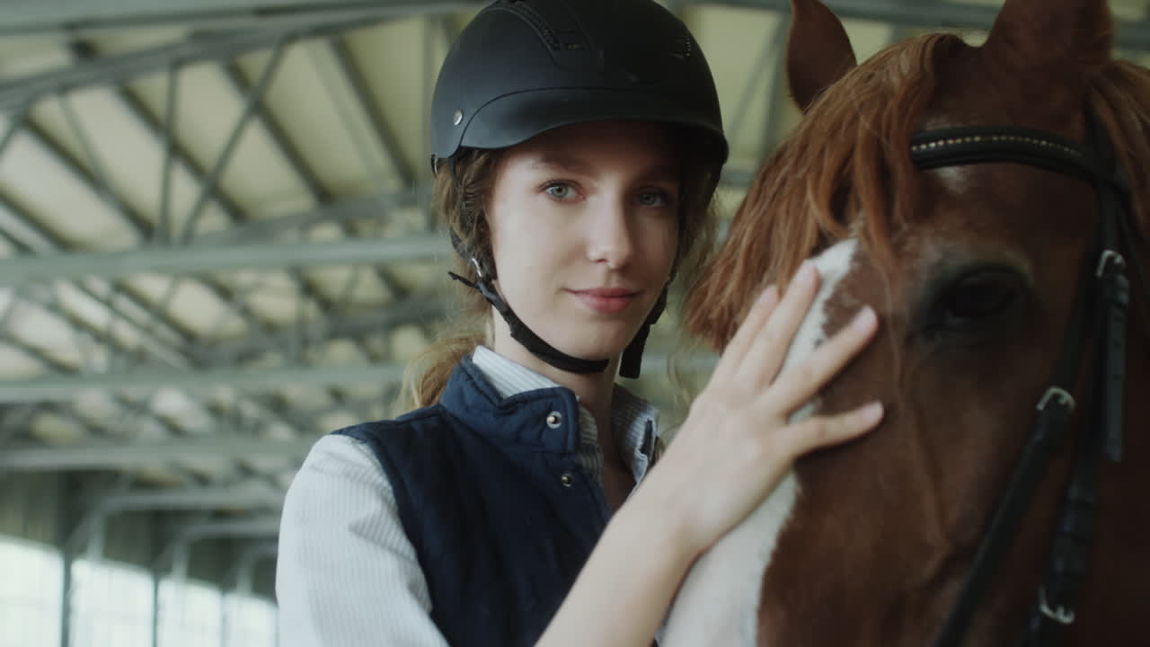 Woman in riding helmet gently petting a horse in a stable