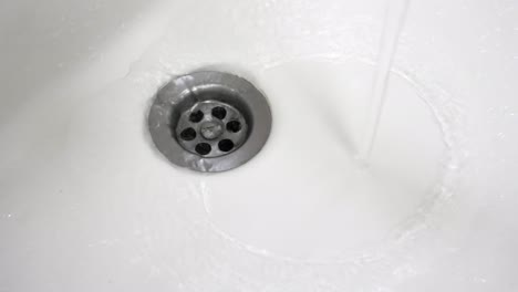 the water flowing from the tap enters the sink drain. close-up shot, 25fps