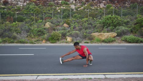 hombre afroamericano realizando ejercicios de estiramiento en la carretera