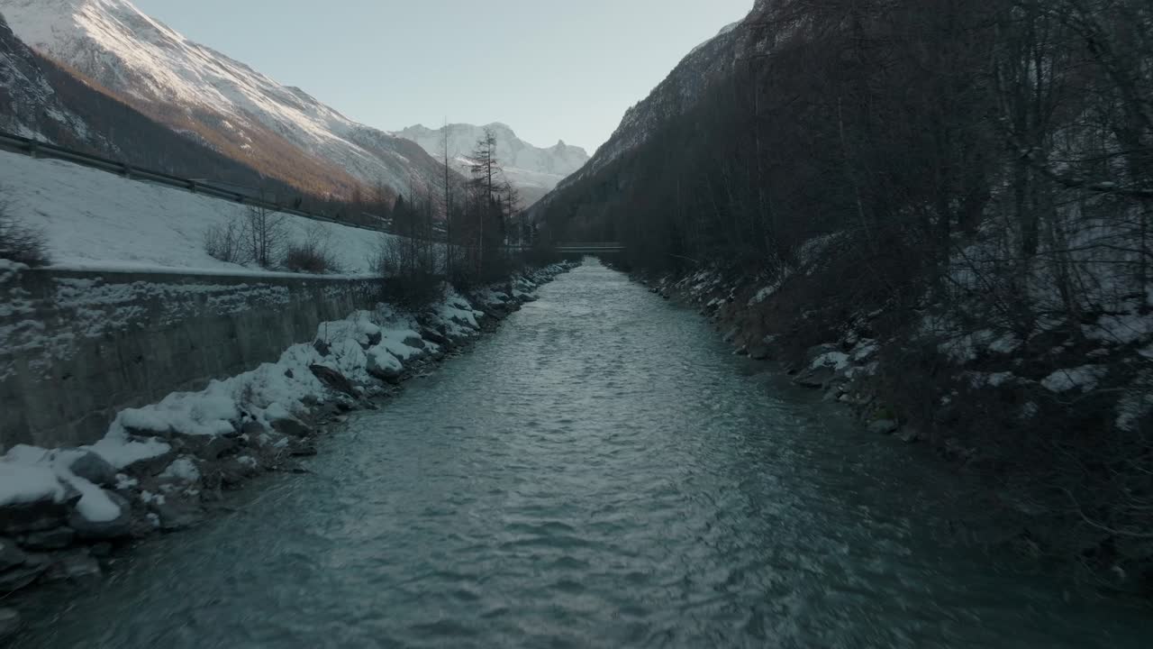 서사시적인 산 파노라마와 함께 스위스 알프스의 강둑에 눈이 내리는 차가운 스위스 흐르는 강물 위에 공중 드론 돌리