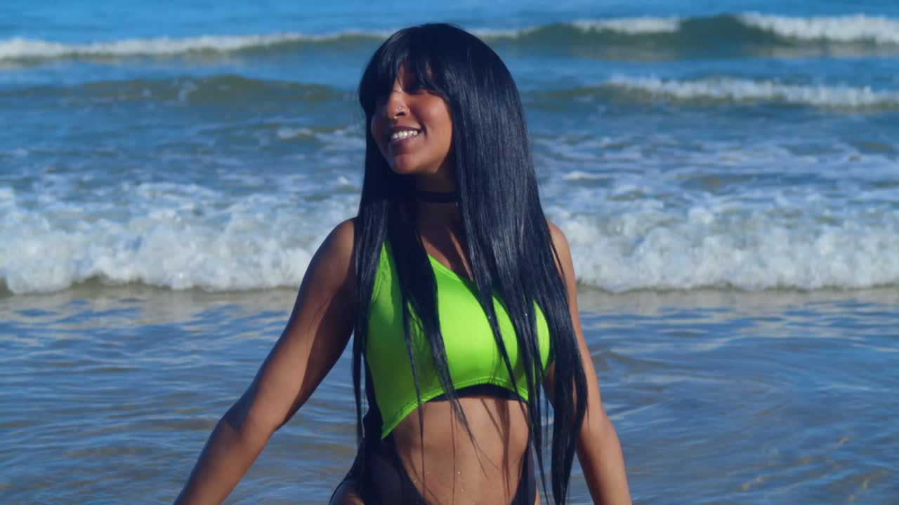 Il sole tropicale brilla su una ragazza che indossa un bikini verde foresta e nero mentre guada tra le onde turchesi trasparenti.