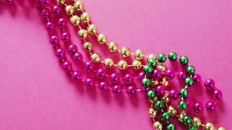 Video-of-pink,-gold-and-green-mardi-gras-carnival-beads-on-pink-background