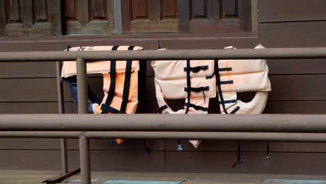 an establishing shot of three old orange faded lifejackets hanging over the railing of a houseboat drying in kanchanaburi, thailand