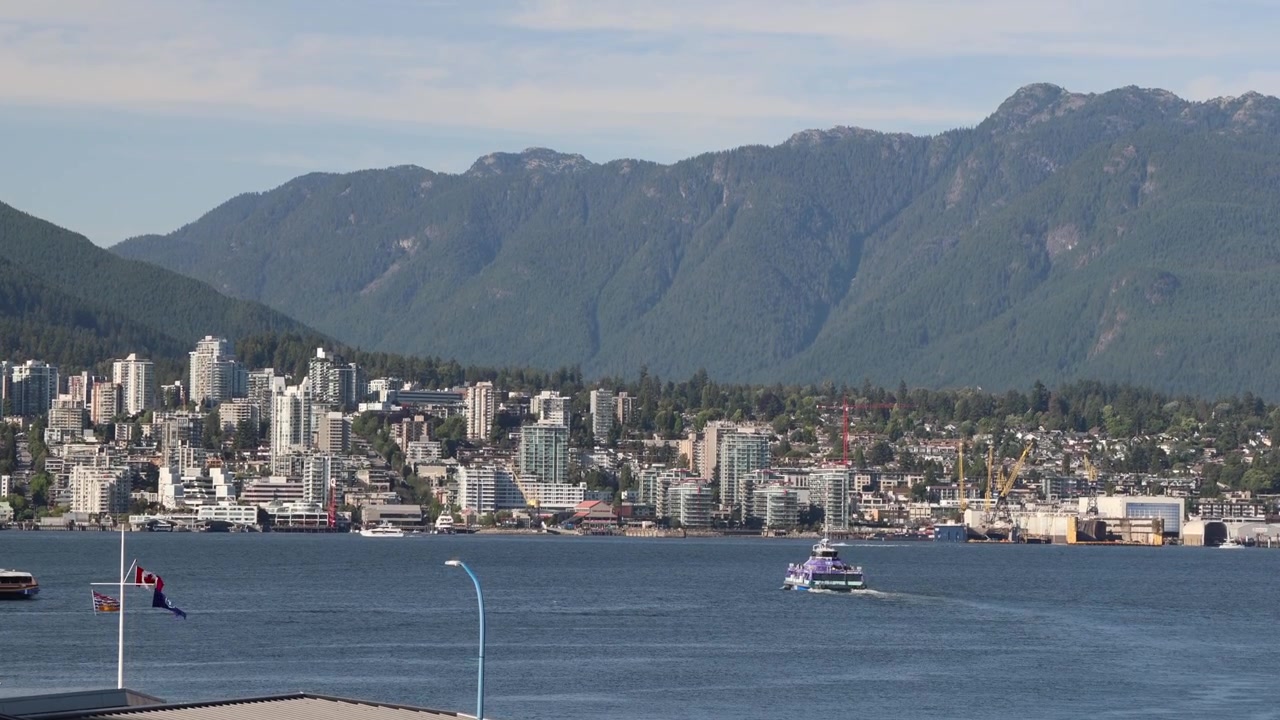 Traghetto in navigazione verso North Vancouver, moderno centro città con grattacieli e montagne.