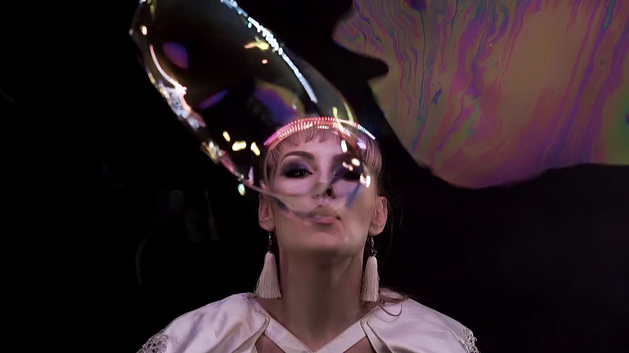Close-up: Truques em câmera lenta com bolhas de sabão. A garota sopra muitas bolhas em direção ao espectador através de uma membrana de sabão.