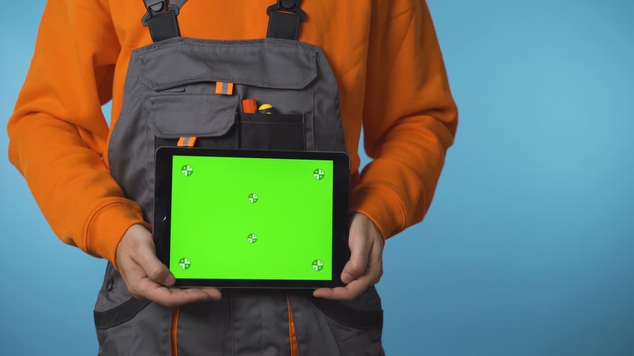 una toma cercana de las manos de un trabajador de la construcción sosteniendo una tableta con pantalla verde.