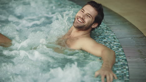 smiling man relaxing in jacuzzi spa indoor. sexy guy resting in whirlpool bath