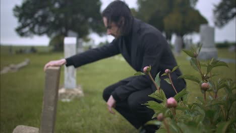 man mourning in cemetery kneels at grave in slow motion