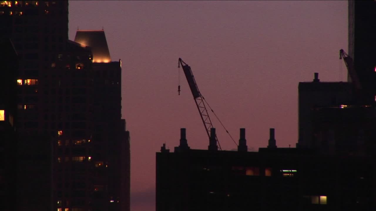 Una grúa de construcción descansa en un tejado en una foto del perfil urbano a la hora dorada.