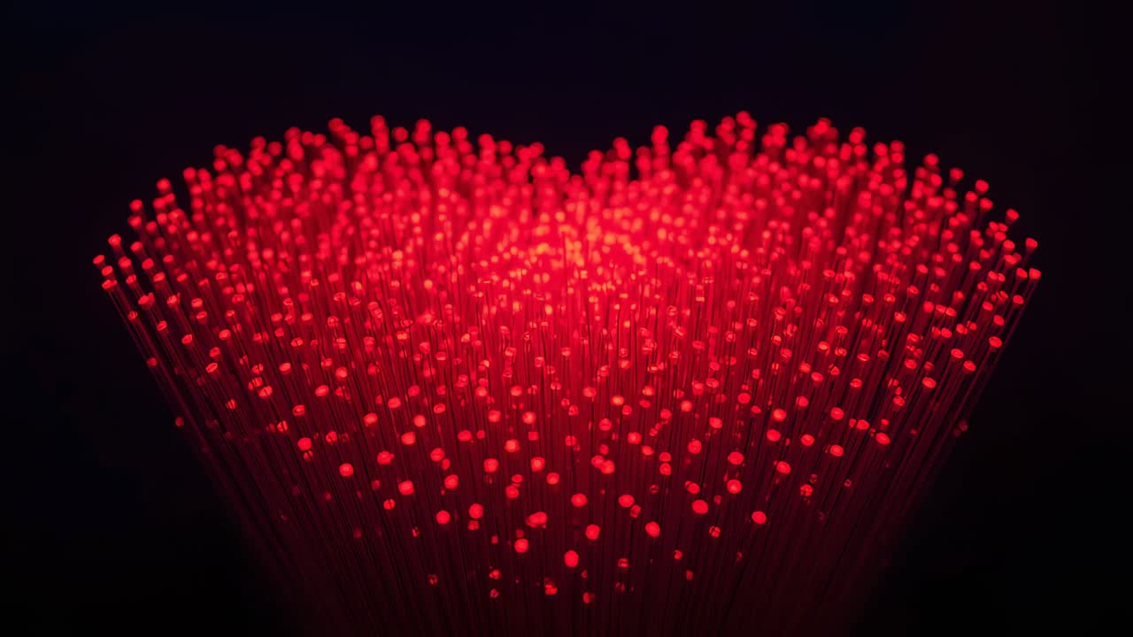 Exibição de filamentos de fibra óptica formando uma parte superior curva e pulsando com pontas de LED vermelhas em um estúdio escuro