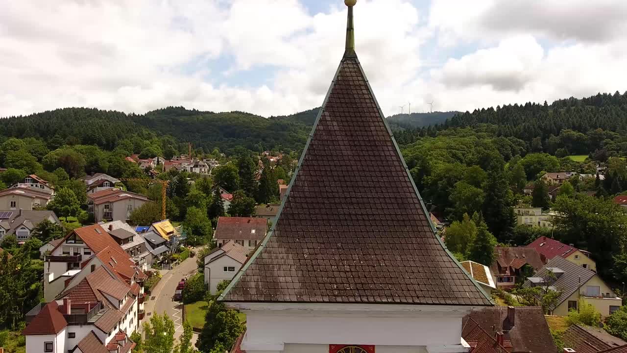 volando sobre la torre de una iglesia, montañas con turbinas de viento en el fondo