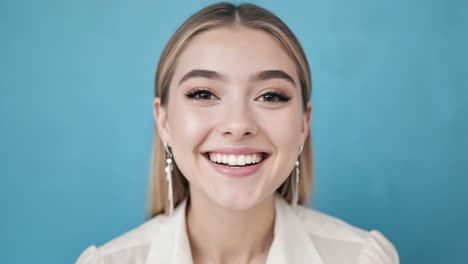 professional businesswoman in white shirt and earrings, radiating joy, smiling brightly against blue studio backdrop, conveying confident, positive workplace attitude