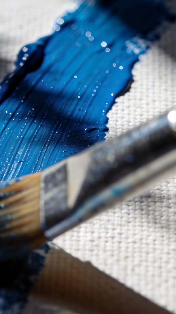 Video verticale: Prendendo un pennello piatto da una goccia di colore, spalmando pittura blu su tela tesa con la ghiera.