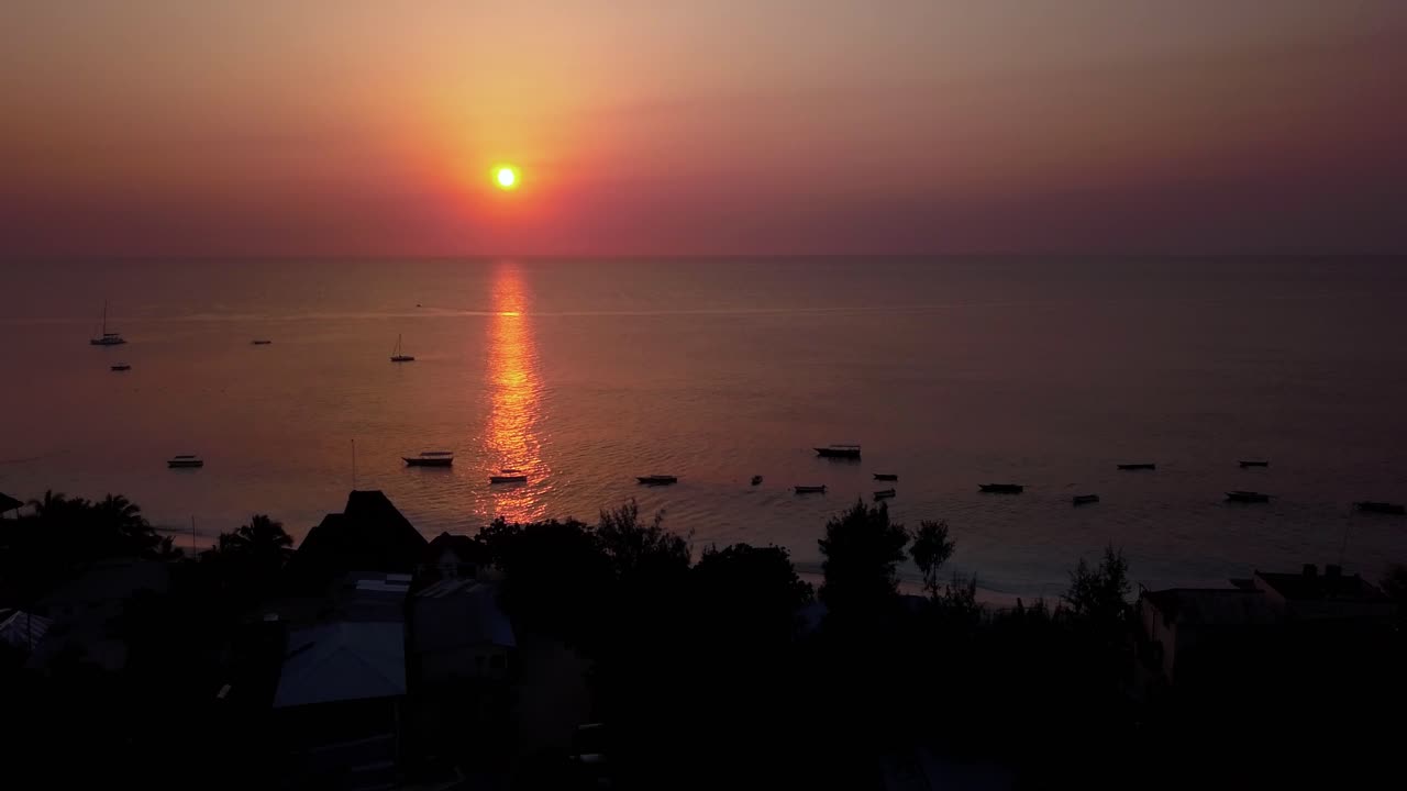 Amazing Sunset Pull back Drone Aerial Over the Ocean with Silhouetted Boats Lining the Shoreline in Popular Tropical Tourist Vacation spot Nungwi Beach, Zanzibar, Unguja, Island in Tanzania