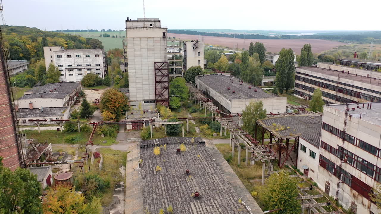 Abandoned factory with many ruined buildings. Old brick thick pipe on empty plant. Deserted industrial territory. Aerial view.