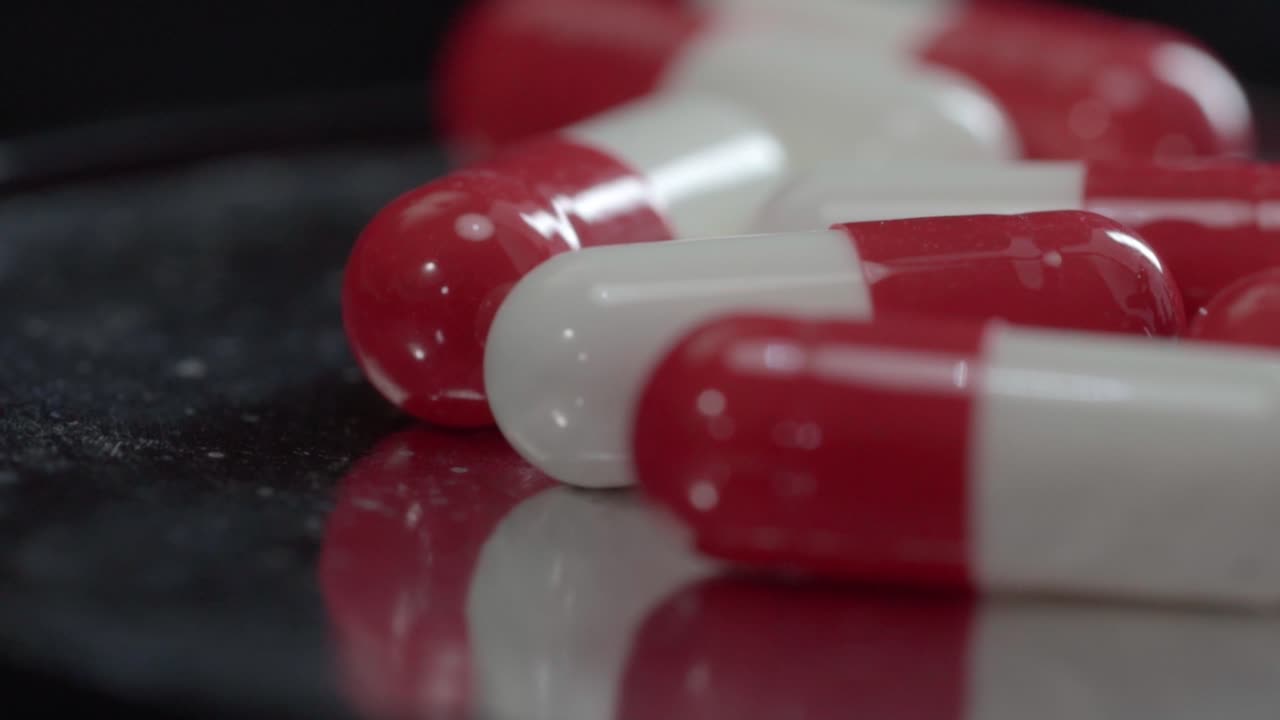 Close up of red and white capsules rotating on reflective glass surface, pharmaceutical product detail
