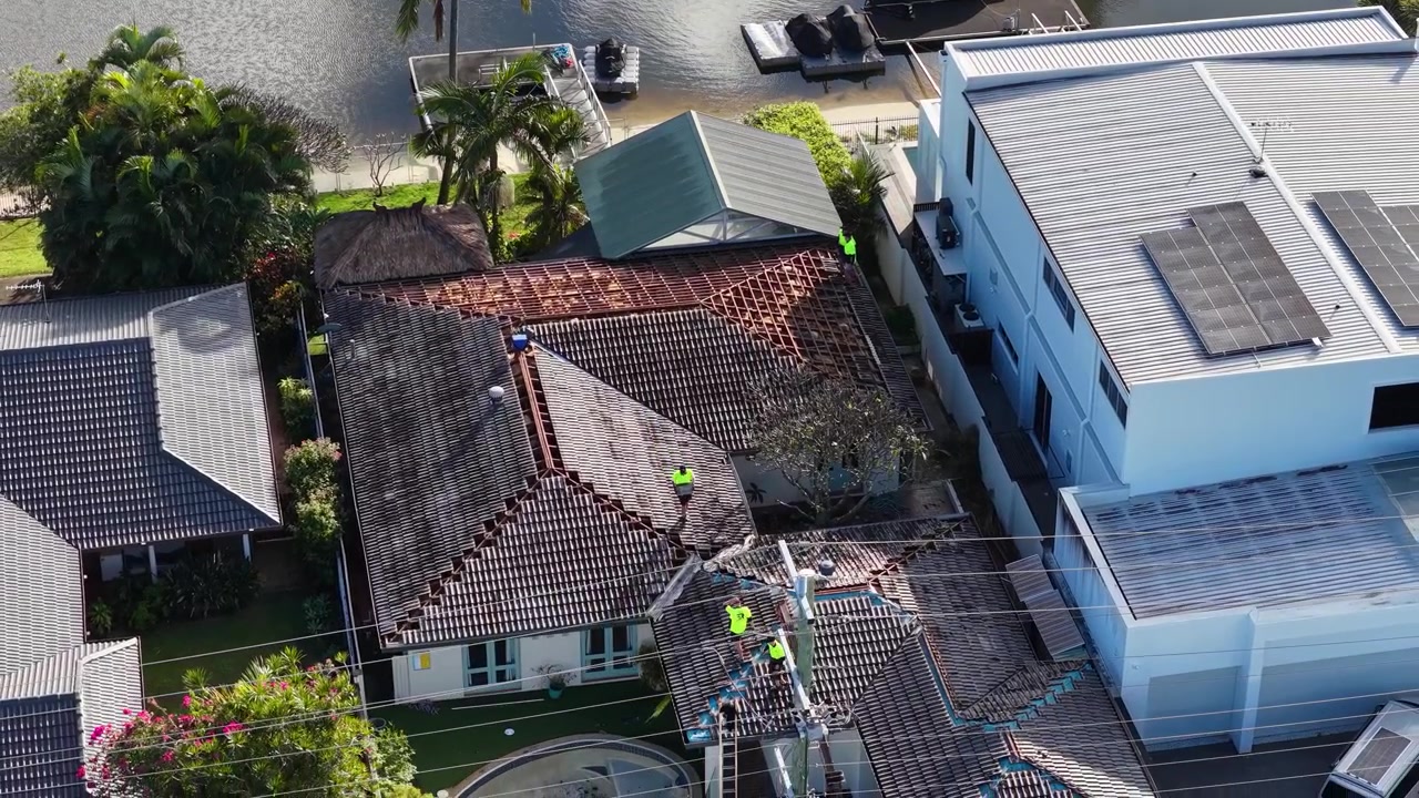 High-angle drone shot of contractors in safety vests renovating a residential roof near water.