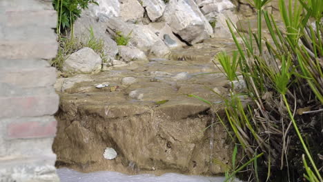 static shot of a miniature waterfall fountain with water streaming to bubbly pond