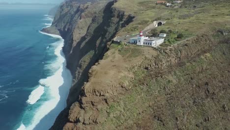 aerial flight backwards gigantic cliff with deep ocean and lighthouse on edge during sunlight